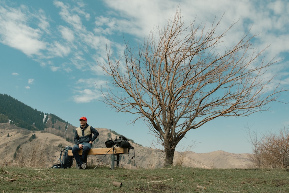 a man sitting on a bench next to a tree