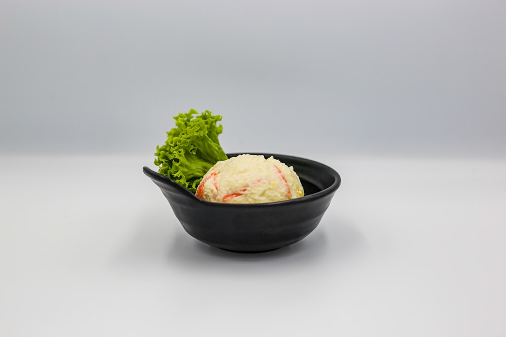 a black bowl filled with lettuce on top of a white table