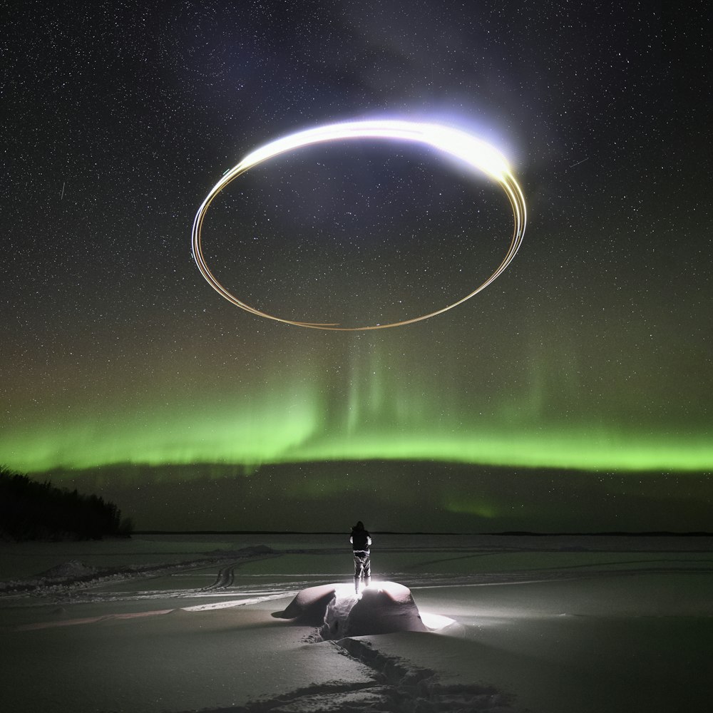 a person standing in the snow under an aurora circle