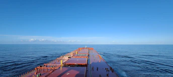 A cargo ship loaded with containers of building materials sailing under a clear blue sky.