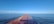 A cargo ship loaded with containers navigating through calm waters under a clear blue sky.