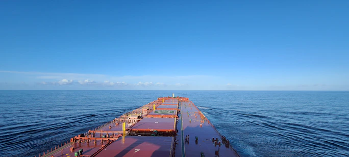 A sleek cargo ship sailing under a clear sky with containers stacked high, symbolizing international shipping.