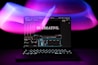 A laptop is displayed with a video editing software open on the screen. The words 'Be Creative.' appear prominently, suggesting a focus on creativity. The background features swirling light patterns in shades of purple, pink, and blue, creating an artistic ambiance.