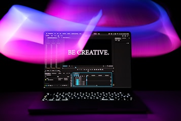 A laptop is displayed with a video editing software open on the screen. The words 'Be Creative.' appear prominently, suggesting a focus on creativity. The background features swirling light patterns in shades of purple, pink, and blue, creating an artistic ambiance.