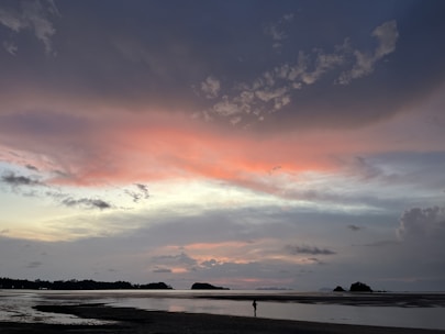 A vibrant photo of a traveler enjoying a sunset on a tropical beach with pink and blue skies.