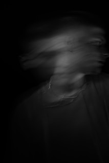 A blurred, ghostly figure of a person captured in motion, creating a sense of mystery and fluidity against a black background.
