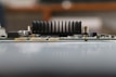A close-up side view of an electronic circuit board featuring a prominent black heat sink with vertical fins. The board contains small electronic components, including resistors and capacitors, with a blurred background.