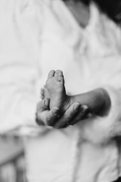 Soft-focus photo of a gentle hand holding a newborn's tiny fingers against a blue and white background.