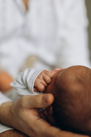 Close-up of a mother gently holding her newborn's hand in a softly lit room.