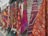 Several colorful and intricately patterned rugs hang side by side against a stone wall. The patterns include geometric shapes and are woven in vibrant colors such as red, orange, purple, blue, and green.