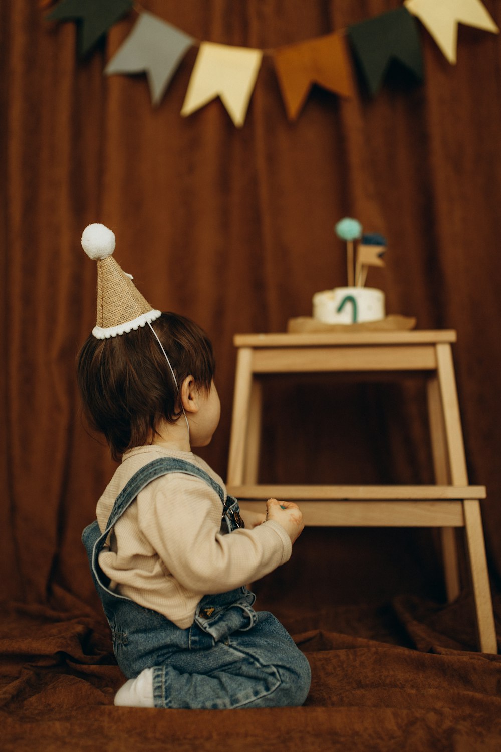 a small child sitting on a bed wearing a birthday hat