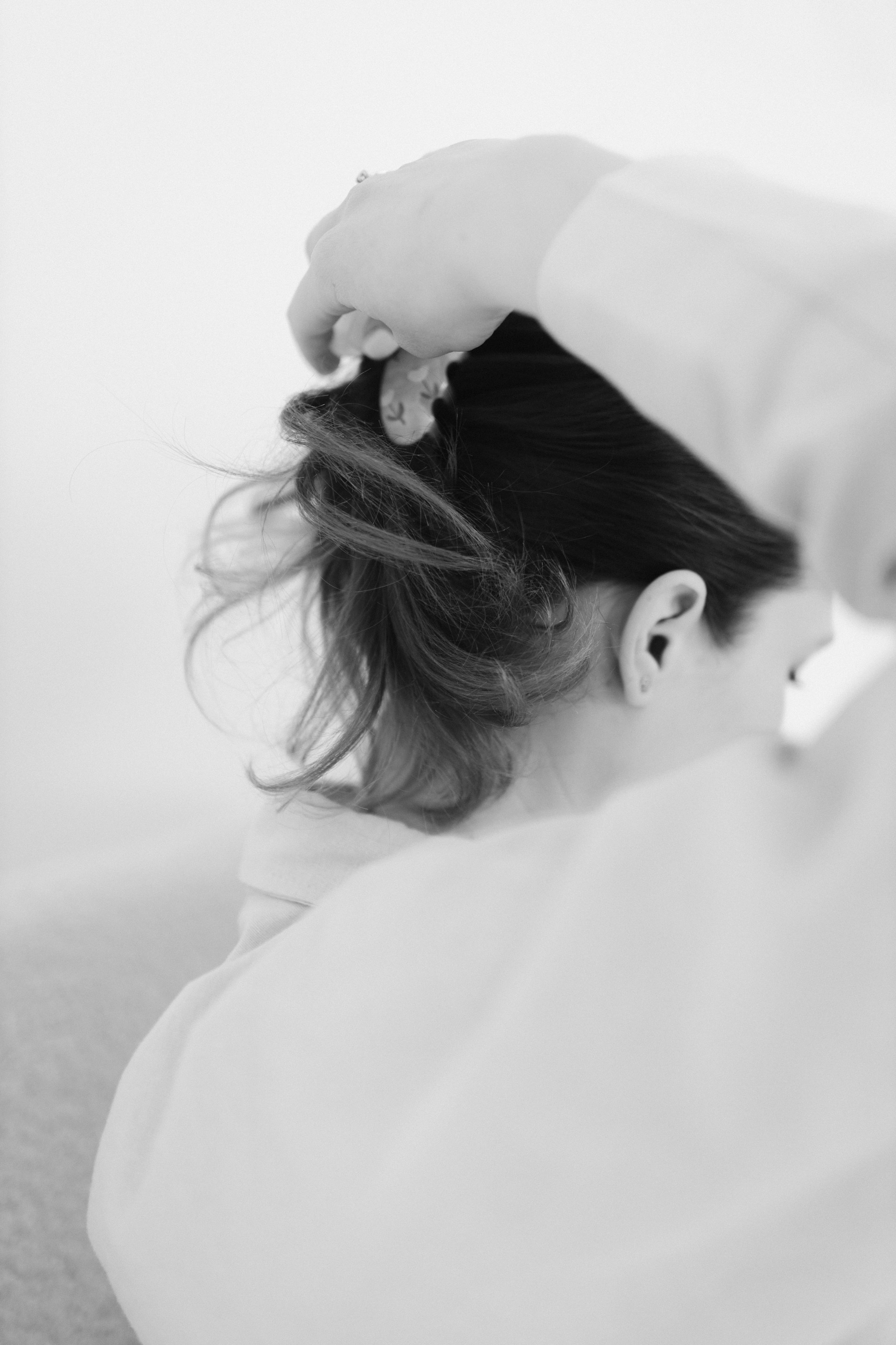 An elegant black-and-white shot capturing a stylist gently placing a bespoke hair topper on a client, emphasizing craftsmanship and attention to detail in a sleek studio setting.