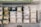 A metal shelf is neatly organized with various labeled plastic containers filled with grains, nuts, and seeds. The labels on the containers suggest careful categorization of contents, with some containers branded as 'wellocks.' The surrounding environment appears to be a storage or kitchen area, with additional metal containers stacked on the right.