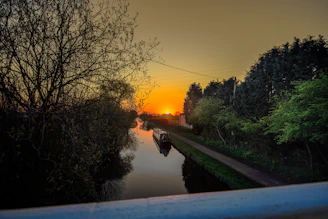 A sleek turquoise all-electric canal boat gliding silently along a classic narrow canal at sunset.