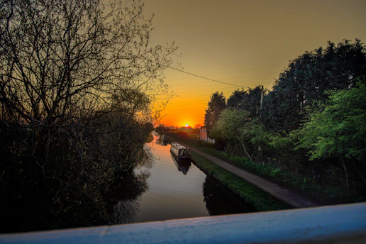 A sleek turquoise all-electric canal boat gliding silently along a classic narrow canal at sunset.
