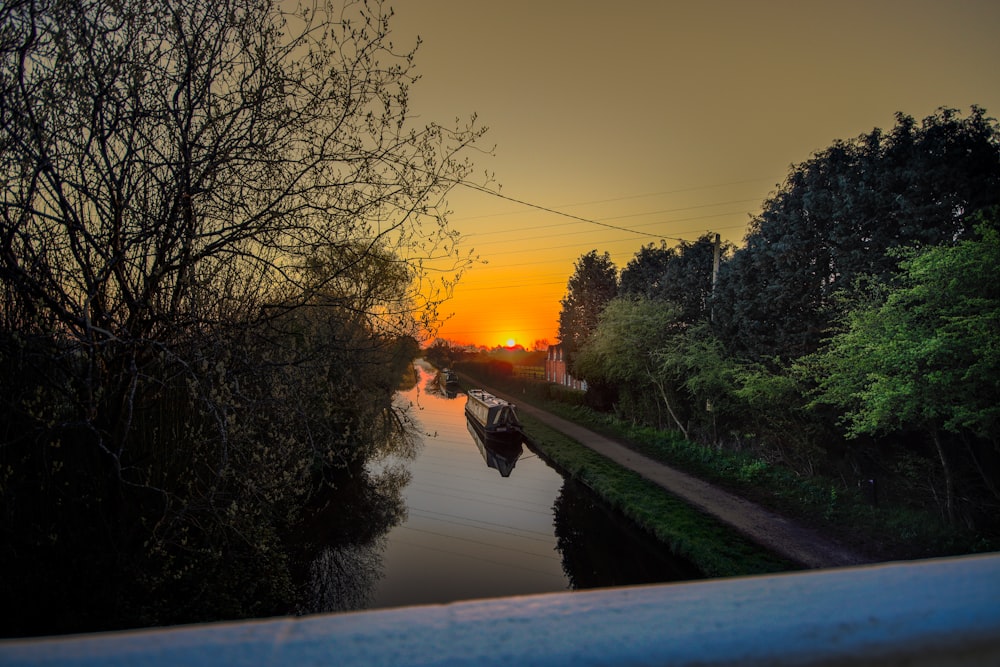 the sun is setting over a canal with a boat in it