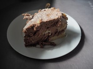 Slice of moist chocolate cake with a dusting of powdered sugar on a beige linen cloth.