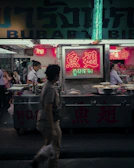 Close-up of hands distributing food packages to people on the street under blue neon lighting.