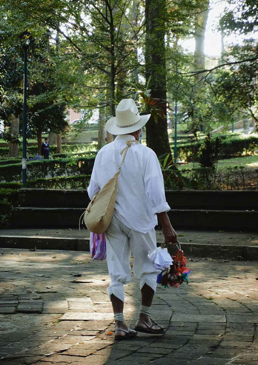 a man in a white hat and white pants walking in a park