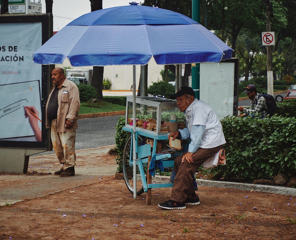 a man sitting on a blue chair under a blue umbrella