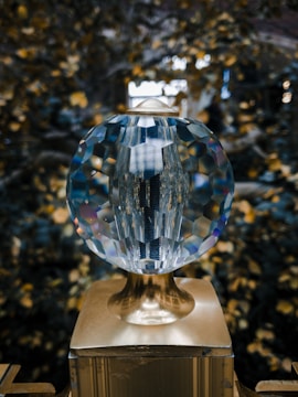A multifaceted crystal orb resting on a metallic stand, against a blurred background with bokeh effects of light. The crystal reflects and refracts light, creating a kaleidoscope of colors.