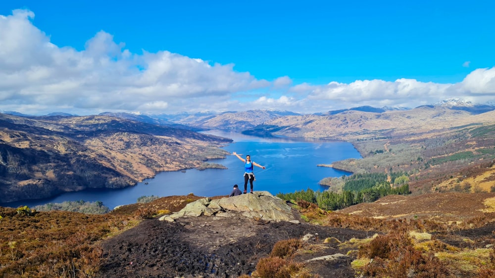 a man standing on top of a mountain next to a lake