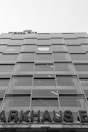 A multi-story glass building with a modern design, featuring a grid of large windows. A partially visible sign at the top reads 'MOTEL ONE', and at the lower portion, a large sign displays 'PARKHAUS'. The structure appears to be utilitarian with straight lines and reflective surfaces.