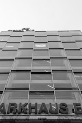 A multi-story glass building with a modern design, featuring a grid of large windows. A partially visible sign at the top reads 'MOTEL ONE', and at the lower portion, a large sign displays 'PARKHAUS'. The structure appears to be utilitarian with straight lines and reflective surfaces.
