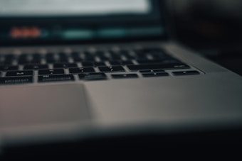 A close-up view of a laptop keyboard and trackpad, with soft lighting creating a moody atmosphere. The focus is on the keys, while the background is blurred, presenting a modern and sleek design.