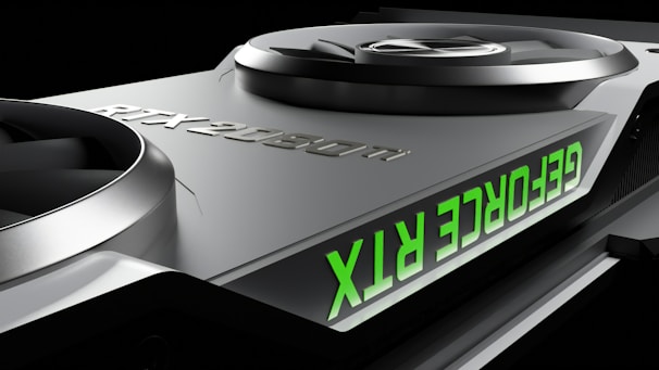 Close-up of a graphics card featuring two large cooling fans and the text 'GEFORCE RTX' displayed in green. The metallic surface has a sleek, modern design with embossed characters 'RTX 2080 Ti'.