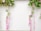 Colorful floral arrangements hang against a white background, featuring a variety of leaves and flowers in shades of green, pink, purple, and white. The arrangement includes cascading pink flowers that hang gracefully alongside vibrant green leaves.