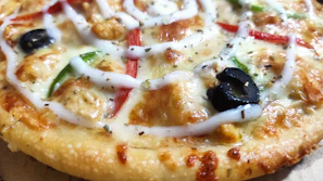 Close-up of a sizzling chicken supreme pizza with melted cheese and fresh herbs