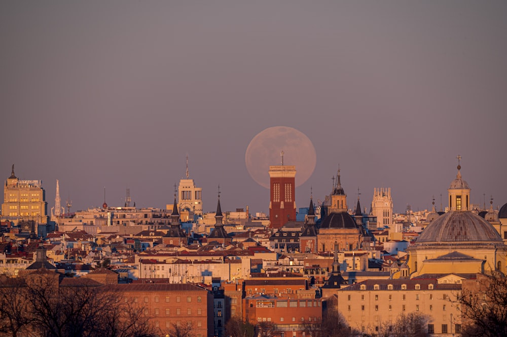 a full moon rising over a city with tall buildings