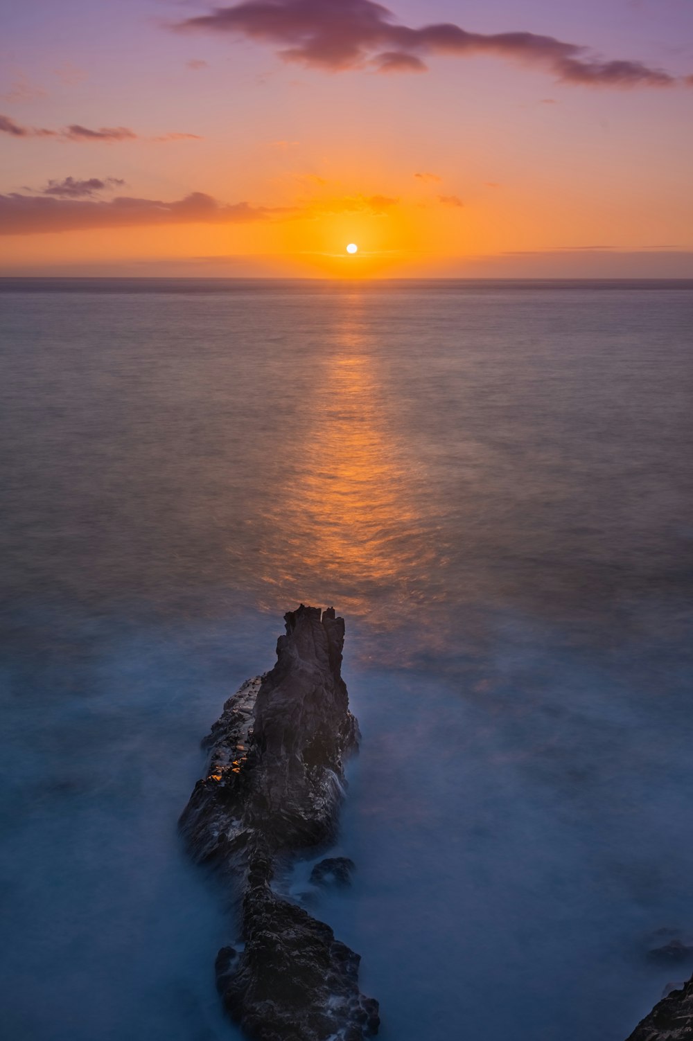 the sun is setting over the ocean with rocks in the foreground