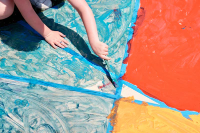 Close-up of a child's hands painting a colorful Bible verse illustration.