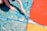 A child's hands are painting a large surface with various sections filled with bold colors, including blue, red, and orange. The painting appears abstract with swirling patterns and sections divided by blue tape.