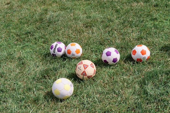 Several soccer balls with different colors and patterns are scattered on a grassy field.