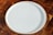 A plain, round, white ceramic plate is placed on a wooden surface with a checkered pattern made up of various shades of brown.