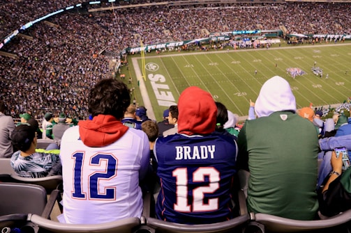 Fans walking into a stadium wearing matching hats and hoodies under bright stadium lights.