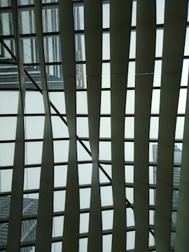 Metallic and glass structures create an abstract geometric pattern against the sky, featuring a grid-like design of intersecting lines and panels.