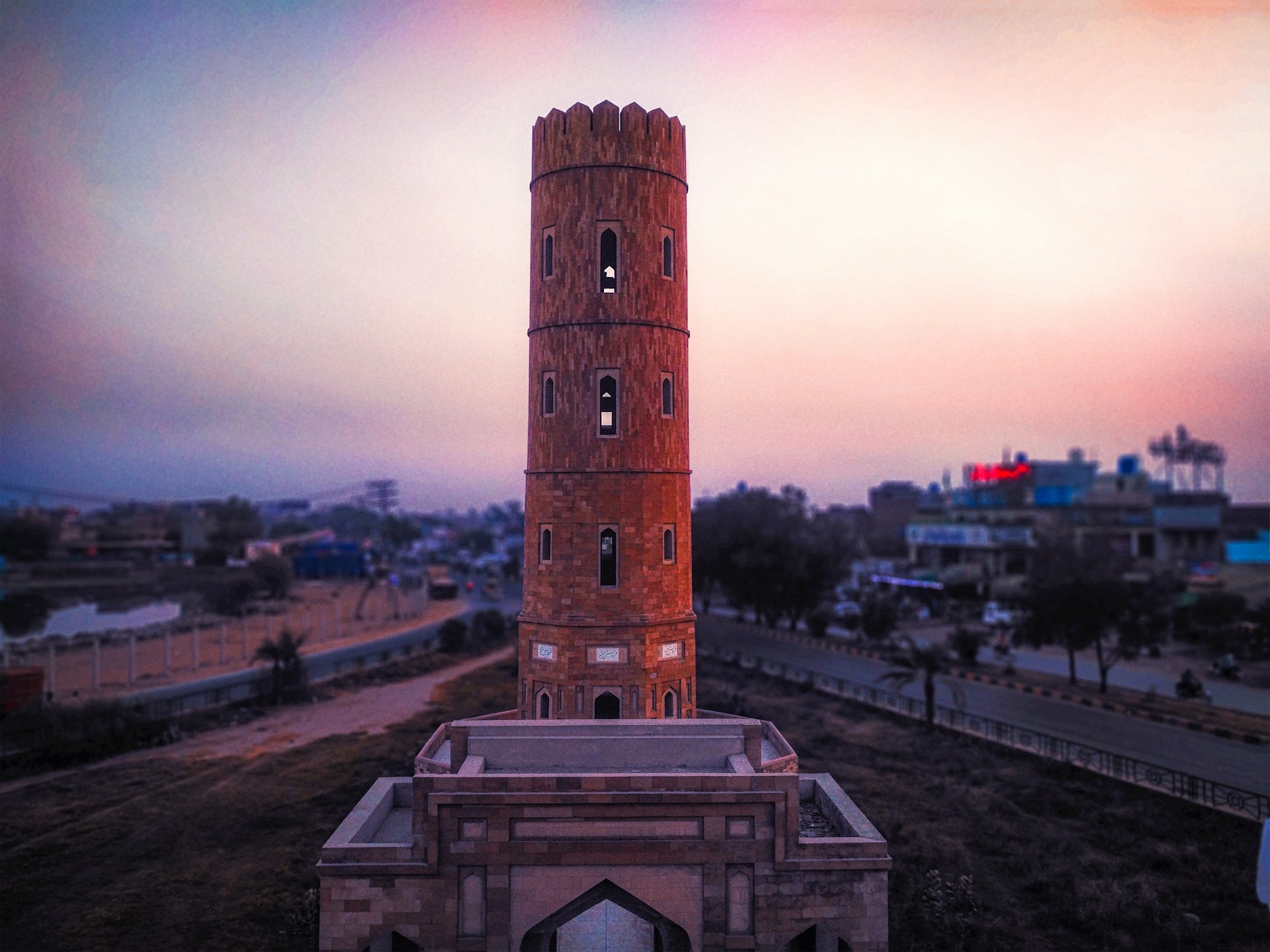 The iconic Markka Watch Tower standing tall against a sunset, framed by lush greenery and modern buildings.
