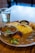 A plate of assorted Indian food with a metal bowl of curry garnished with herbs. The plate includes yellow rice, purple cabbage, carrots, and various vegetables. A glass of water is placed next to the plate on a wooden table.