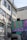 A building exterior with large, industrial pipes running along the side. The upper floors feature windows with metal bars and a visible roof overhang. A colorful mural covers part of the lower wall, displaying the large letters 'ALG' over a patterned background.