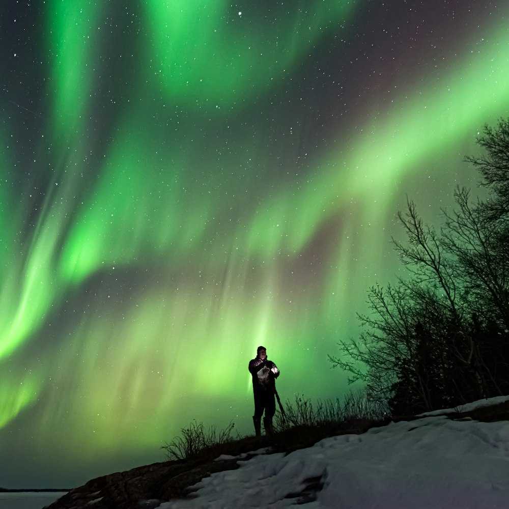 a man standing on top of a snow covered slope under a green and purple sky