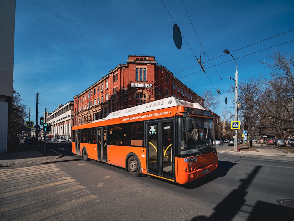 an orange bus driving down a street next to a tall building