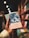 A hand is holding a colorful book titled 'Os Lusiadas' by Luis de Camões. The book cover features an intricate design, with a blend of dark blues and light hues. The background shows a blurred bookshelf filled with other books, creating a cozy and inviting atmosphere.