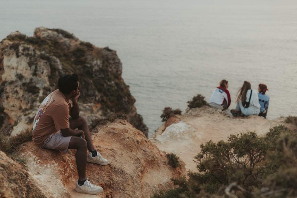 a group of people sitting on top of a cliff next to the ocean