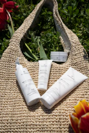 Close-up of natural skincare products with green leaves on a camel-colored fabric.