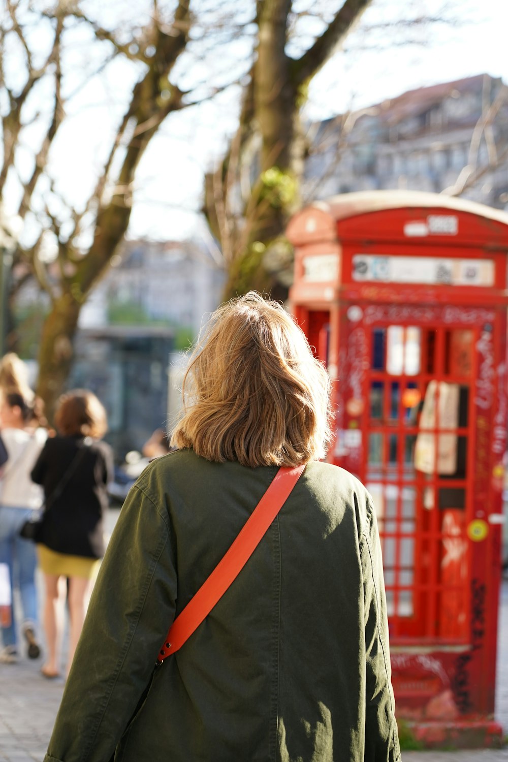 a woman walking down a street past a red phone booth