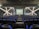 A modern theater with rows of blue and black seats facing a stage. The walls have geometric patterns with illuminated lines creating an 'X' shape. The stage is empty except for a few people standing near the back.